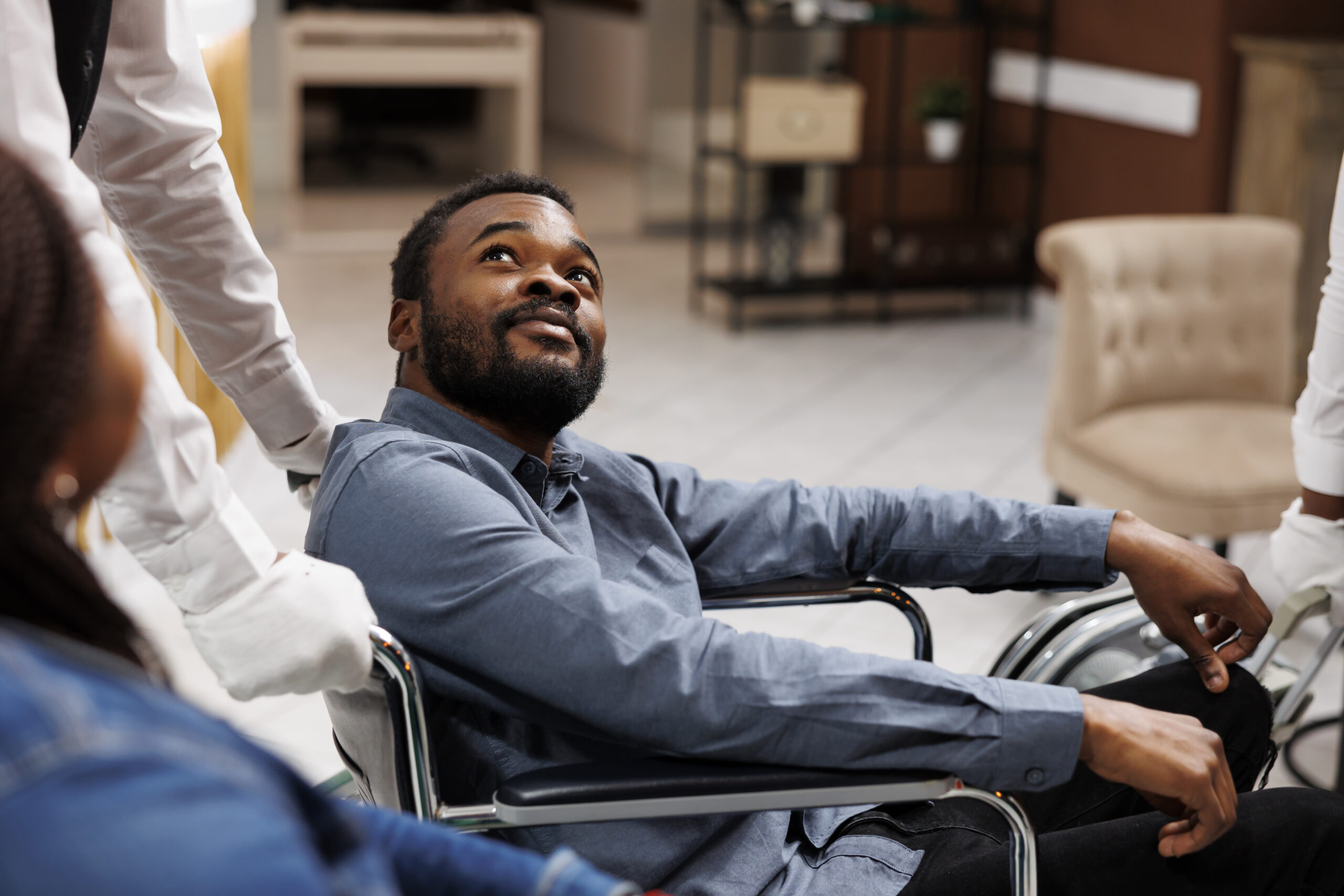 Happy young African American man using wheelchair during travel, receiving help and assistance in wheelchair-friendly and accessible hotel. People with mobility impairment and traveling